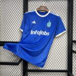 camiseta el barrio - kings league Camiseta oficial de 'El Barrio' de la King League en color azul, con logo de InfoJobs en el centro y detalles en dorado en el cuello y las mangas, colgada en una rejilla negra.