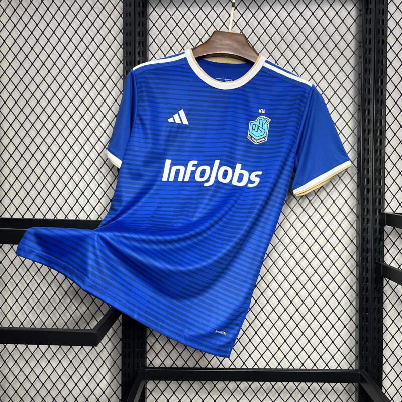 camiseta el barrio - kings league Camiseta oficial de 'El Barrio' de la King League en color azul, con logo de InfoJobs en el centro y detalles en dorado en el cuello y las mangas, colgada en una rejilla negra.