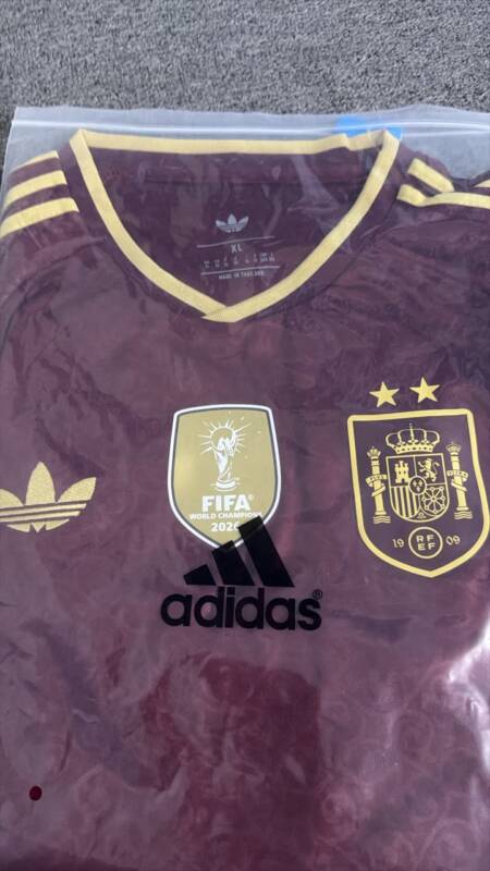 Foto real de la camiseta granate de España con dos estrellas dentro de una bolsa transparente